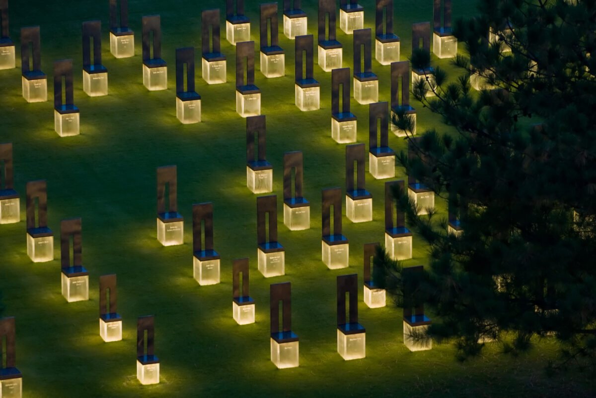 Rows of empty bronze and stone chairs on glass bases at the Oklahoma City National Memorial, lit from below at dusk