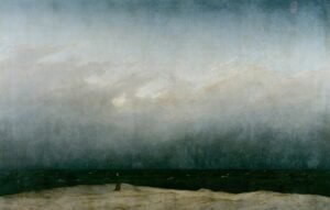 A tiny figure in a dark robe stands alone on a pale strip of dune beside a dark sea, under a vast grey sky that fills most of the painting.