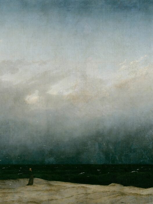 A tiny figure in a dark robe stands alone on a pale strip of dune beside a dark sea, under a vast grey sky that fills most of the painting.
